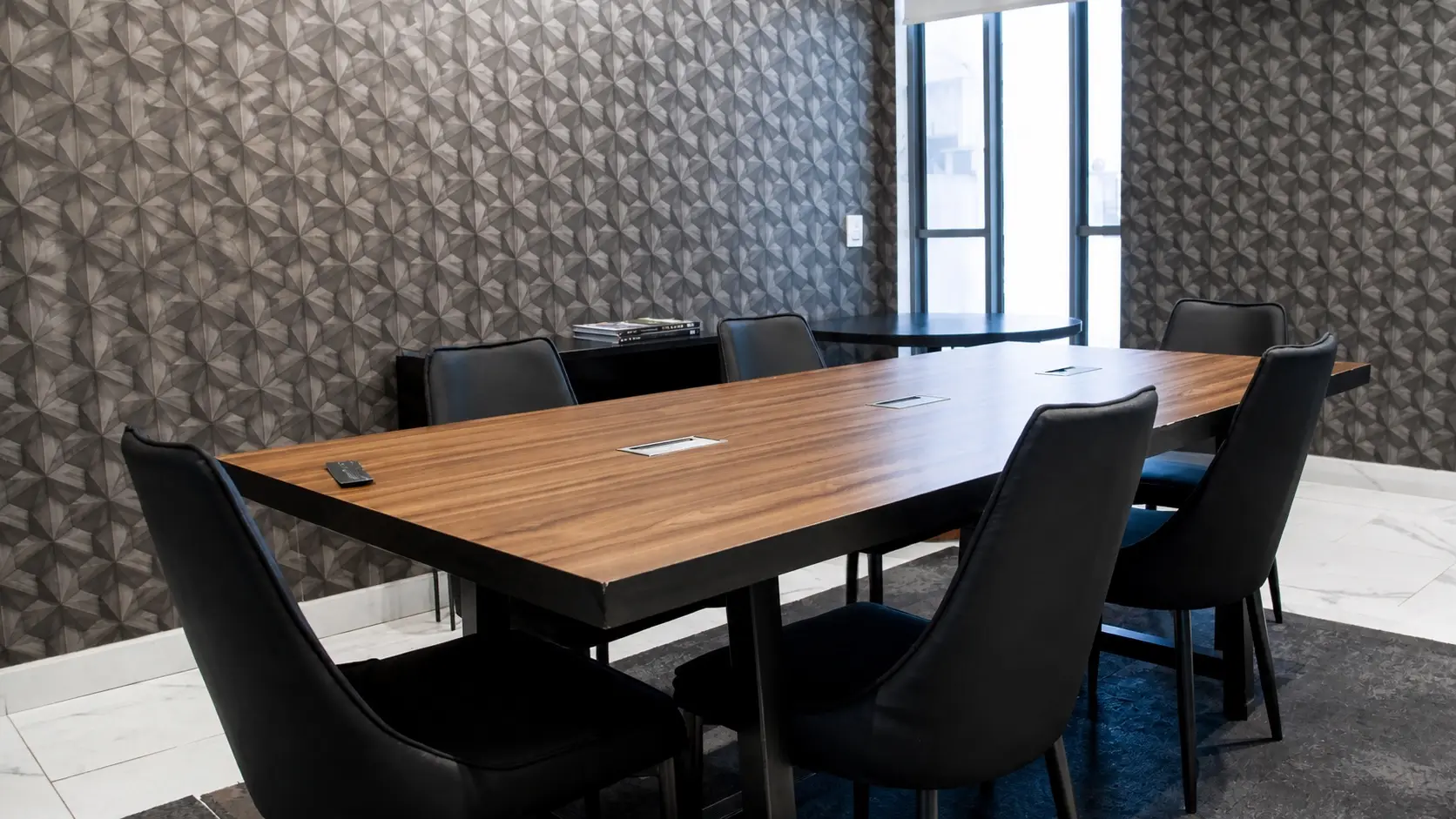 Sala de juntas de Concordia Patrimonial: mesa de madera para seis personas, sillas negras y muro con relieve geométrico.
